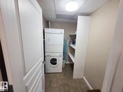 Dedicated laundry area featuring a stacked washer and dryer, tile flooring, and integrated shelving - 