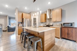 Modern kitchen featuring an expansive center island with seating, pendant lighting, stainless steel appliances, light wood-finish cabinetry, and wood-finish flooring - 