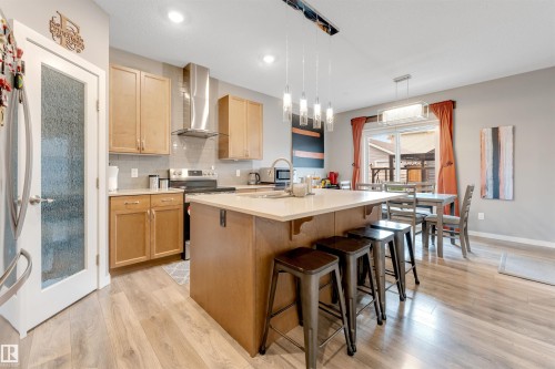 Kitchen featuring an island with built-in cabinetry, stainless steel appliances, light wood-finish flooring, and a sliding glass door to the exterior - 2652 Maple Way, Edmonton, AB - Indoor Photo Showing Kitchen With Upgraded Kitchen