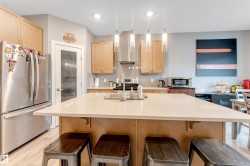 Spacious kitchen featuring a large central island with light-toned countertop, stainless steel appliances, wood-finish cabinetry, and recessed lighting - 