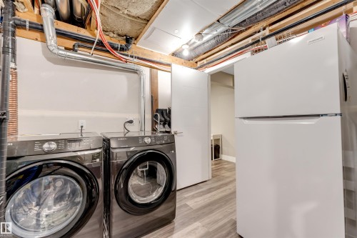 Dedicated laundry area featuring a front-loading washer and dryer set, wood-finish flooring, and a full-size refrigerator - 2652 Maple Way, Edmonton, AB - Indoor Photo Showing Laundry Room