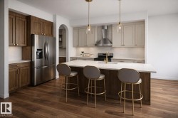 Contemporary kitchen featuring a large center island with integrated sink, two-tone cabinetry, stainless steel appliances, a tile backsplash, and wood-finish flooring - 