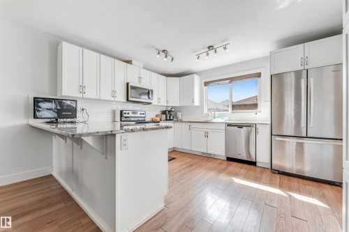 Bright kitchen featuring white cabinetry, stainless steel appliances, wood-finish flooring, a tile backsplash, and a window above the sink - 1536 21 Street, Edmonton, AB - Indoor Photo Showing Kitchen With Stainless Steel Kitchen With Upgraded Kitchen