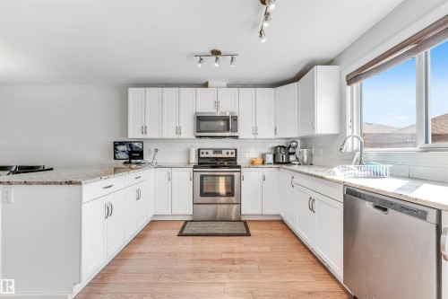 U-shaped kitchen featuring white cabinetry, stainless steel appliances, granite-finish countertops, subway tile backsplash, and wood-finish flooring - 1536 21 Street, Edmonton, AB - Indoor Photo Showing Kitchen With Stainless Steel Kitchen With Upgraded Kitchen