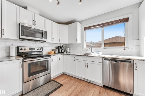 Bright kitchen featuring white cabinetry, a subway tile backsplash, stainless steel appliances, granite-finish countertops, and wood-finish flooring - 1536 21 Street, Edmonton, AB - Indoor Photo Showing Kitchen With Stainless Steel Kitchen