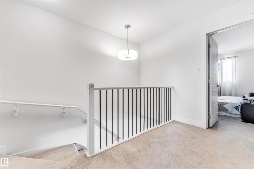 Carpeted landing featuring a modern ceiling light fixture, white walls, and a staircase with white wood newel posts and black metal balusters - 1536 21 Street, Edmonton, AB - Indoor