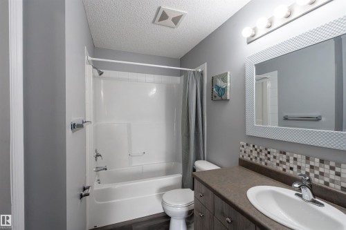 Full bathroom featuring a shower-tub combination, wood-finish vanity with an integrated sink, and mosaic tile backsplash - 4407 23 Street, Edmonton, AB - Indoor Photo Showing Bathroom