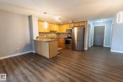 Open-concept living area featuring wood-finish flooring, a kitchen with light wood cabinetry, stainless steel appliances, a tiled backsplash, and a breakfast bar - 