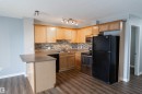 Kitchen featuring light wood cabinetry, a mosaic tile backsplash, dark countertops, and wood-finish flooring - 4407 23 Street, Edmonton, AB  - Indoor Photo Showing Kitchen With Double Sink 