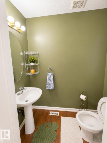Pedestal sink with chrome faucet, oval mirror, and three-bulb vanity light fixture - 704 83 Street, Edmonton, AB - Indoor Photo Showing Bathroom