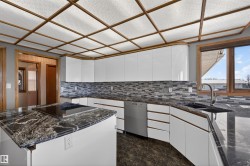 Modern kitchen featuring high-gloss white cabinetry, dark stone countertops, and a mosaic tile backsplash - 