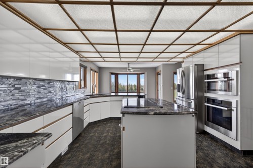 Modern kitchen featuring white cabinetry, dark stone countertops, a mosaic tile backsplash, and stainless steel appliances including a built-in oven and microwave - 19403 Fort Road, Edmonton, AB - Indoor Photo Showing Kitchen With Upgraded Kitchen