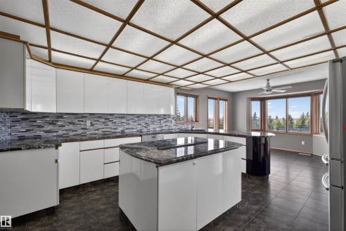 Kitchen featuring a grid-patterned ceiling, white cabinetry, dark stone countertops, and a gray-toned mosaic tile backsplash - 19403 Fort Road, Edmonton, AB - Indoor Photo Showing Kitchen With Upgraded Kitchen