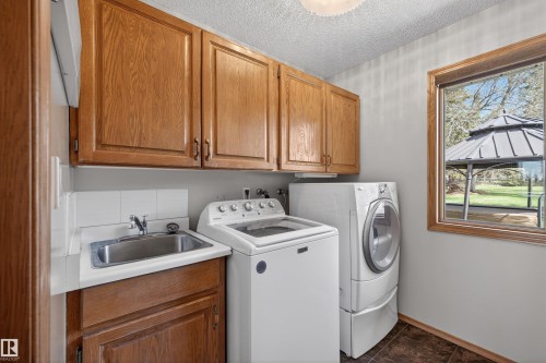 Dedicated laundry room featuring wood cabinetry, a utility sink with white tile backsplash, and a window providing natural light - 19403 Fort Road, Edmonton, AB - Indoor Photo Showing Laundry Room