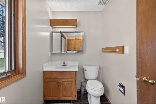 Bathroom featuring a wood-framed window, vanity with integrated sink, wall-mounted medicine cabinet, and a white toilet - 19403 Fort Road, Edmonton, AB - Indoor Photo Showing Bathroom