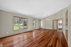 Spacious interior featuring wood-finish flooring, multiple windows, a decorative chandelier, and vaulted ceilings - 
