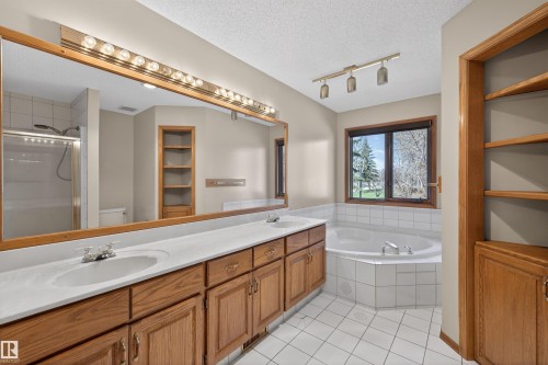 Bathroom featuring a double vanity with wood cabinetry and white countertops, a large framed mirror with overhead lighting, a built-in corner bathtub with white tile surround, and a separate glass-enclosed shower - 19403 Fort Road, Edmonton, AB - Indoor Photo Showing Bathroom
