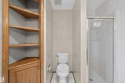 Corner built-in shelving with a lower cabinet, a toilet, and a glass-enclosed shower with white tiled walls - 