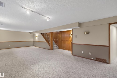 Spacious lower level featuring light-toned carpeting, a wood staircase with balusters, and track lighting - 19403 Fort Road, Edmonton, AB - Indoor Photo Showing Other Room