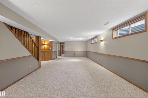 Expansive carpeted room featuring a wooden staircase and paneling - 19403 Fort Road, Edmonton, AB - Indoor Photo Showing Other Room