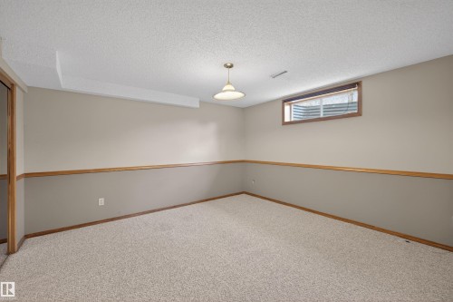 Carpeted room featuring two-tone wall paint with wood trim, a window with wood trim, and a ceiling-mounted light fixture - 19403 Fort Road, Edmonton, AB - Indoor Photo Showing Other Room