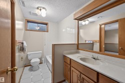 Bathroom featuring a single vanity with a white countertop and integrated sink, wood-finish cabinetry, a framed wall mirror, and hexagonal floor tiling - 
