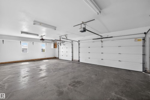 Spacious garage featuring two overhead doors with automatic openers, a durable concrete floor, multiple windows providing natural light, and fluorescent overhead lighting - 19403 Fort Road, Edmonton, AB - Indoor Photo Showing Garage