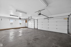Spacious garage featuring two overhead doors with automatic openers, a durable concrete floor, multiple windows providing natural light, and fluorescent overhead lighting - 
