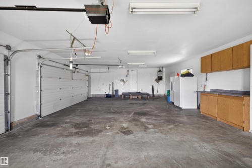 Spacious garage featuring two overhead doors, concrete flooring, and built-in wood-finish cabinetry with a countertop - 19403 Fort Road, Edmonton, AB - Indoor Photo Showing Garage