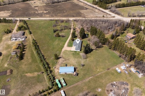 Property with a single-story residence featuring a dark grey roof and light-colored siding, positioned on an expansive lot with mature evergreen trees and cleared green space - 19403 Fort Road, Edmonton, AB - Outdoor With View
