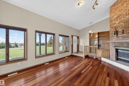Spacious living area featuring rich wood-finish flooring, a prominent brick fireplace with a white hearth, and built-in shelving - 19403 Fort Road, Edmonton, AB - Indoor With Fireplace