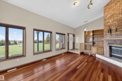 Spacious living area featuring rich wood-finish flooring, a prominent brick fireplace with a white hearth, and built-in shelving - 
