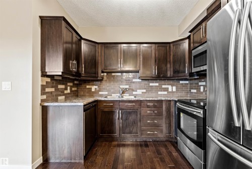Kitchen featuring dark wood-finish cabinetry, stainless steel appliances, and a patterned tile backsplash - 316 10520 56 Avenue Nw, Edmonton, AB - Indoor Photo Showing Kitchen With Stainless Steel Kitchen