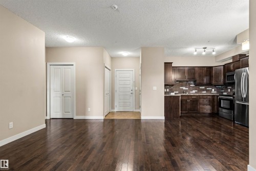 Open-concept living space featuring wood-finish flooring, a kitchen with dark cabinetry, stainless steel appliances, and a mosaic tile backsplash - 316 10520 56 Avenue Nw, Edmonton, AB - Indoor Photo Showing Kitchen With Stainless Steel Kitchen