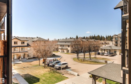 Community grounds featuring a circular drive, mature deciduous trees, a manicured lawn, and multi-story residential buildings with pitched roofs - 316 10520 56 Avenue Nw, Edmonton, AB - Outdoor