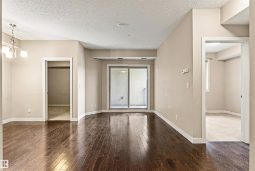 Spacious living area featuring dark wood-finish flooring, neutral wall tones, white baseboards, and a sliding glass door leading to an outdoor balcony - 316 10520 56 Avenue Nw, Edmonton, AB - Indoor Photo Showing Other Room