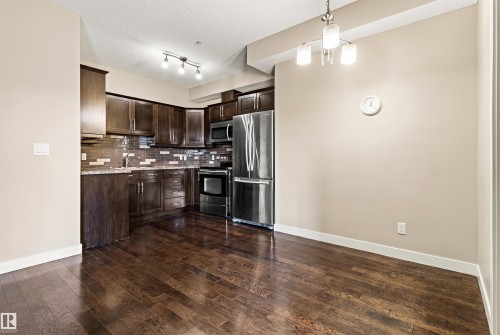 Open-concept kitchen and dining area featuring rich wood-finish flooring, dark wood cabinetry, and stainless steel appliances - 316 10520 56 Avenue Nw, Edmonton, AB - Indoor Photo Showing Kitchen With Stainless Steel Kitchen