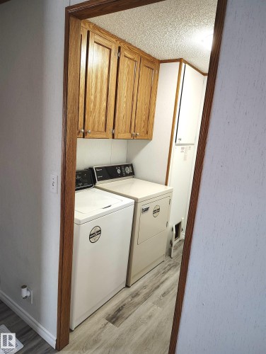 Dedicated laundry area featuring wood-finish cabinetry and wood-look flooring - 109-4819 51 Ave, Millet, AB - Indoor Photo Showing Laundry Room