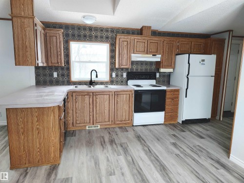 Kitchen featuring wood-finish cabinetry, light countertops, and a full suite of appliances - 109-4819 51 Ave, Millet, AB - Indoor Photo Showing Kitchen With Double Sink