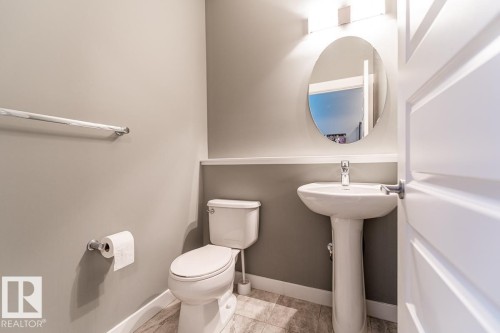 Pedestal sink with chrome faucet, oval mirror, and wall-mounted vanity lighting - 9748 205 Street, Edmonton, AB - Indoor Photo Showing Bathroom