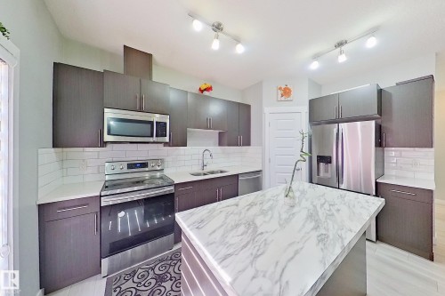 Modern kitchen featuring a central island with a stone-finish countertop, dark wood-finish cabinetry, stainless steel appliances, subway tile backsplash, and track lighting - 1221 27 Street, Edmonton, AB - Indoor Photo Showing Kitchen