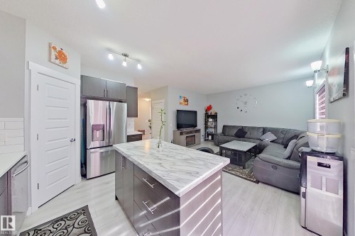 Open-concept living space featuring light wood-finish flooring, a kitchen island with a light-toned countertop, stainless steel appliances, dark cabinetry, and white subway tile backsplash - 1221 27 Street, Edmonton, AB - Indoor