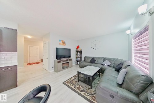 Open concept living space featuring light wood-finish flooring, a contemporary entertainment center with an integrated electric fireplace, large window with horizontal blinds, and recessed lighting - 1221 27 Street, Edmonton, AB - Indoor Photo Showing Living Room
