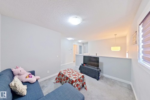 Carpeted loft area with a partial wall overlooking a lower level, featuring a rectangular window with horizontal blinds, a flush-mount ceiling light, and a modern pendant fixture - 1221 27 Street, Edmonton, AB - Indoor