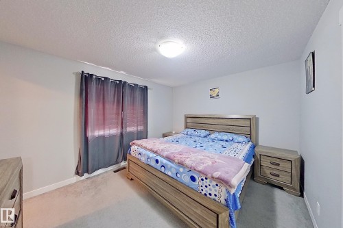 Carpeted room with a textured ceiling, a flush mount light fixture, white baseboards, and a window with dark curtains - 1221 27 Street, Edmonton, AB - Indoor Photo Showing Bedroom