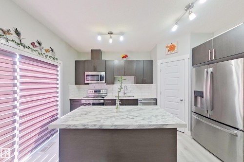 Modern kitchen featuring an island with a light-toned countertop, stainless steel appliances, dark wood-finish cabinetry, a subway tile backsplash, and light wood-finish flooring - 1221 27 Street, Edmonton, AB - Indoor Photo Showing Kitchen With Upgraded Kitchen
