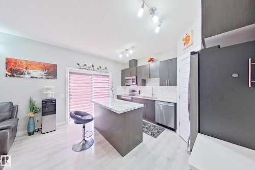 Modern kitchen featuring dark cabinetry, stainless steel appliances, white subway tile backsplash, and a central island with a light-toned countertop - 1221 27 Street, Edmonton, AB - Indoor Photo Showing Kitchen
