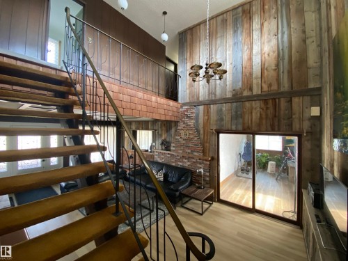 Two-story living area featuring a vaulted ceiling with wood paneling, a brick fireplace, and sliding glass door access - 12137 50 Street, Edmonton, AB - Indoor Photo Showing Other Room