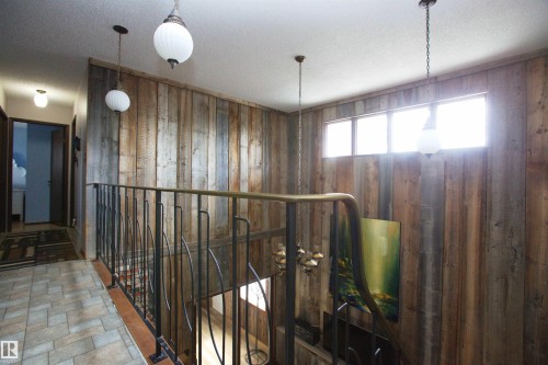 Wood-paneled accent wall with transom windows and three suspended globe light fixtures - 12137 50 Street, Edmonton, AB - Indoor Photo Showing Other Room
