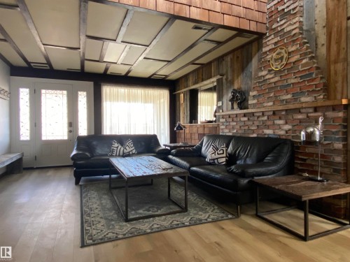 Living area featuring a brick fireplace, wood-plank accent wall, and light wood-finish flooring - 12137 50 Street, Edmonton, AB - Indoor Photo Showing Living Room